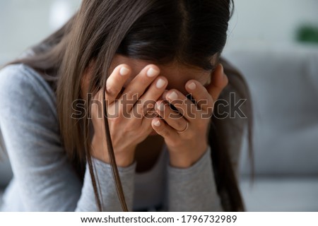 Close up unhappy young woman hiding face in hands, feeling desperate cheated hopeless alone indoors. Upset millennial girl crying, suffering from consequences of wrong decision, depression concept.