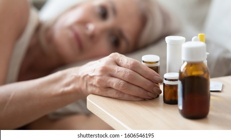 Close up of unhealthy mature woman lying in bed feel sick take medicines from bedside table to relieve symptoms, ill lonely senior female having meds pills suffer from flu, elderly healthcare concept - Powered by Shutterstock