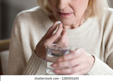 Close Up Of Unhealthy Middle Aged Woman Suffers From Pain, Holding Pill And Glass Of Still Water Feels Ill Taking Medicine, Cropped Image. Disease Prevention And Treatment Of Old Mature People Concept