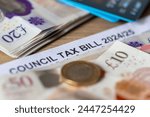 A close up of a United Kingdom local authorities Council Tax bill with bank notes, Pound coin and bank cards.