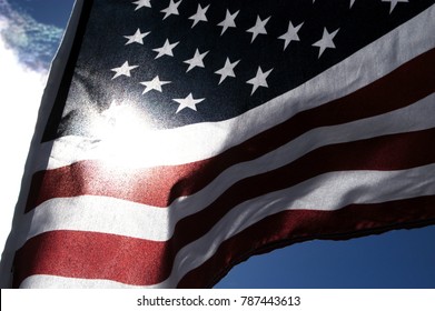 Close Up Of A United States Flag Outside In The Sun. Detail Of The Stars On Blue Background Of The American Flag Waving In The Wind. Looking At The Sun Through A US Flag, Noise/film Grain Filter Added