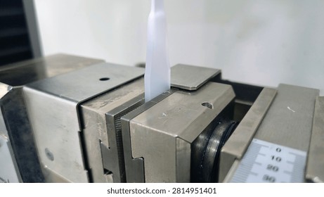 Close up of universal testing machine grip holding a plastic specimen for tensile test. Material mechanical strength evaluation in laboratory