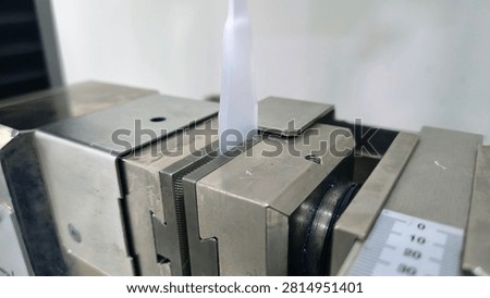 Close up of universal testing machine grip holding a plastic specimen for tensile test. Material mechanical strength evaluation in laboratory