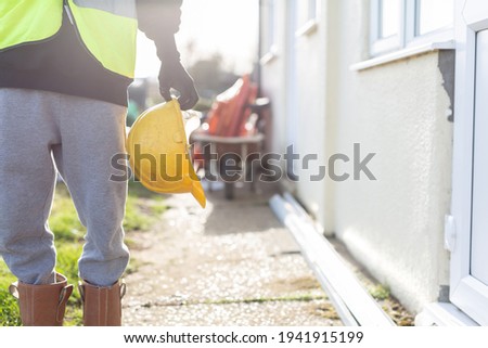 A close up of a unknown builder wearing a high visibility vest and holding a hard hat. Builder, safety, building site, laborer concept