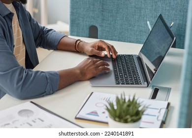 Close up of unrecognizable black man typing at laptop keyboard while using laptop at workplace, copy space
