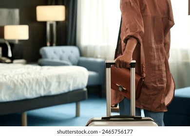 Close up of unrecognizable Black woman entering hotel room and holding suitcase upon travelling to resort copy space