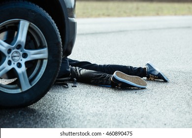 Close Up of Unrecognizable Car Accident Fatality - Bottom Half and Legs of Young Teenage Boy Car Accident Victim Lying on Wet Road Pavement in front of Stopped Vehicle - Powered by Shutterstock