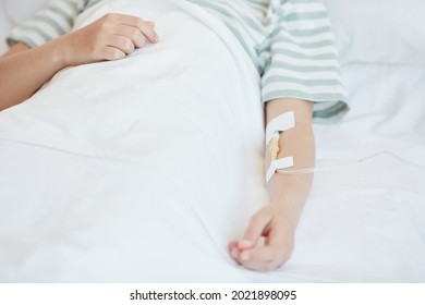 Close Up Of Unrecognizable Child In Hospital Bed With Focus On IV Drip In Arm, Copy Space