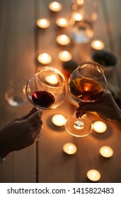 Close Up Of Unrecognizable Couple Enjoying Romantic Dinner Clinking Wine Glasses And By Wooden Table Lit By Candle Light, Copy Space