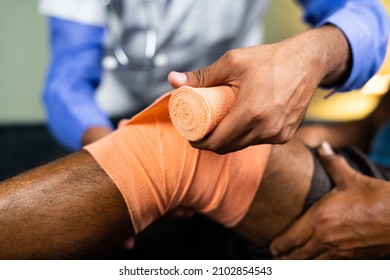 Close Up Of Unrecognizable Doctor Unwrapping Stretch Bandage After Recovering From Knee Sprain Or Joint Paint From Patient - Concept Of Knee Sprain And Muscle Injury Treatment.