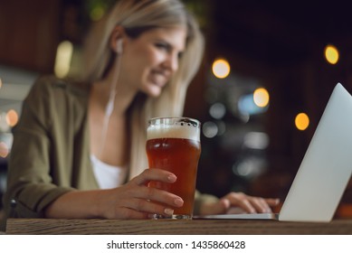 Close up of unrecognizable happy woman holding glass of  beer while surfing the net on laptop in a bar