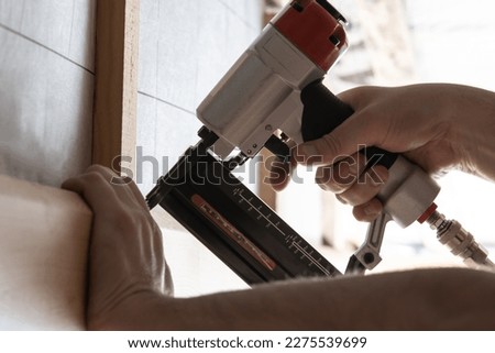 Close up unrecognizable male hands using pneumatic nailer, stapler gun for wooden plank outdoors. Clipping with metal nails and staples, making layout on wooden timber. Build house, carpenter job
