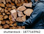 Close up of unrecognizable man dressed in jacket carries bundle of firewood, going to make fire outdoor. Winter is coming.