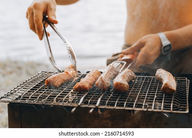 Close up unrecognizable man hands smoked pork meat on outdoor barbecue. Chef putting juicy sausage on grill in forest park outdoor. Preparing dinner lunch Eating summer food in backyard countryside.