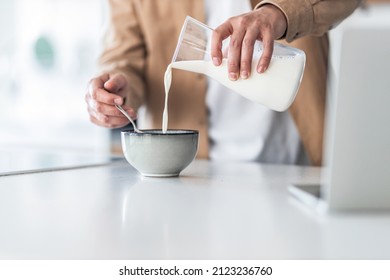 Close up of unrecognizable man pouring fresh milk into a bowl while preparing himself breakfast in the kitchen. Copy space. - Powered by Shutterstock