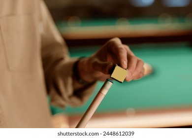 Close up of unrecognizable man using chalk cube on cue stick while playing pool copy space