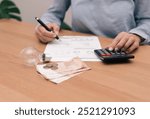 close up of unrecognizable Person analyzing electricity bill with calculator, light bulb and money on desk