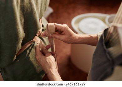 Close up of unrecognizable senior woman helping client tying apron during pottery class in art studio - Powered by Shutterstock