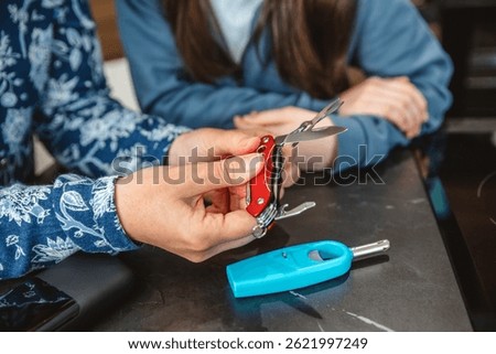 Close up of unrecognizable woman checking multitool knife while explaining 72 hours emergency kit to teenage girl with lighter and powerbank. Alert, foresight and self sufficiency family strategy.