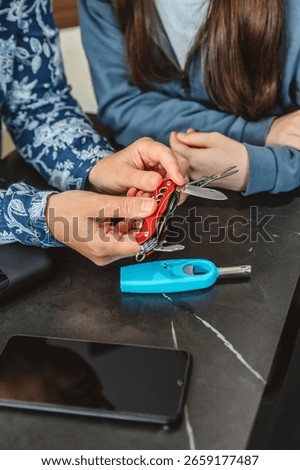 Close up of unrecognizable woman checking multitool knife while explaining 72 hours emergency kit to girl with battery charger, lighter and mobile. Alert, foresight and self sufficiency strategy.