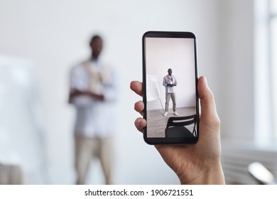 Close up of unrecognizable woman taking photo of African-American businessman standing by whiteboard, focus on smartphone screen, copy space - Powered by Shutterstock