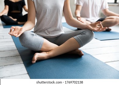 Close up unrecognizable young fit woman sitting on sport floor mat in open hips restorative padmasana lotus pose with folded in mudra symbol hands on knees, enjoying meditating at group yoga class. - Shutterstock ID 1769702138