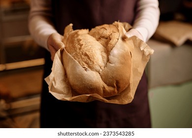 Close up of unrecognizable young woman carefully holding fresh bread in artisan bakery, copy space - Powered by Shutterstock