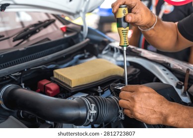 Close up unrecognized auto mechanic using screwdriver to tighten a screw after installing car air flow sensor in auto repair shop