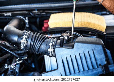 Close up unrecognized auto mechanic using screwdriver to tighten a screw after installing car air flow sensor in auto repair shop