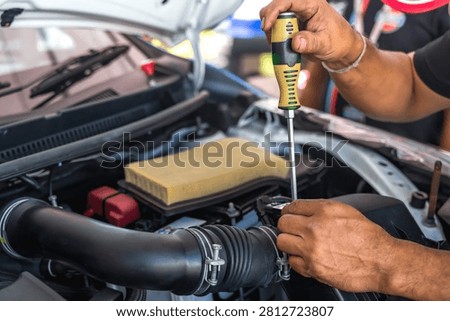 Close up unrecognized auto mechanic using screwdriver to tighten a screw after installing car air flow sensor in auto repair shop