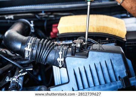 Close up unrecognized auto mechanic using screwdriver to tighten a screw after installing car air flow sensor in auto repair shop