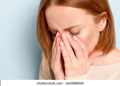 Close uo portrait of young woman has problem with contact lenses, rubbing her swollen eyes due to pollen, dust allergy. Dry eye syndrome, watery, itching, blue background.
