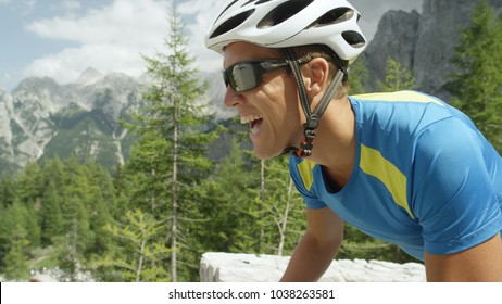 CLOSE UP: Active Caucasian Male With Sunglasses Enduring In Intense Bike Race Over Sunny Mountain Pass. Determined Road Cyclist Biking Uphill A Challenging Mountain Road On A Picturesque Summer Day.