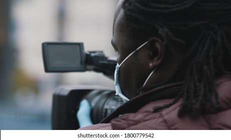 Close up, african black videographer with medikal mask looking through the viewfinder on video camera . High quality photo