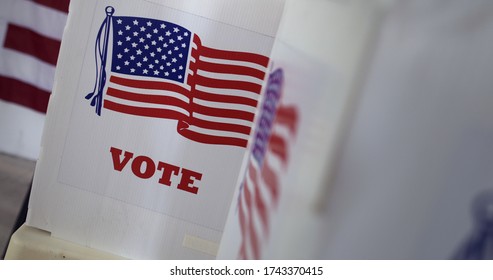Close up, angled view across voting booths at polling station in United States during election. Large US flag on wall behind.