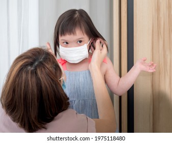 Close up, Asian mother putting medical face mask for young disabled child, down syndrome or trisomy 21 daughter during pandemic outbreak of Coronavirus or Covid 19.