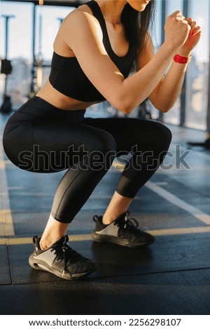 Close up. Athletic girl in black sportswear, leggings and top doing squats in the gym.