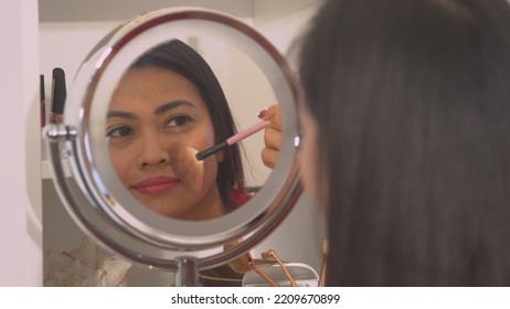 CLOSE UP: Attractive Young Asian Woman Applying Powder Bronzer To Beautify Her Face. Mirror Reflection Of A Pretty Lady Using Brush To Apply Face Blush. Female Person Taking Care Of Her Fresh Look.