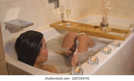 CLOSE UP: Back view shot of beautiful lady with smartphone while chilling in bath. Young female person enjoying and relaxing in bubble bath while using smartphone for checking feed on social media. - Powered by Shutterstock