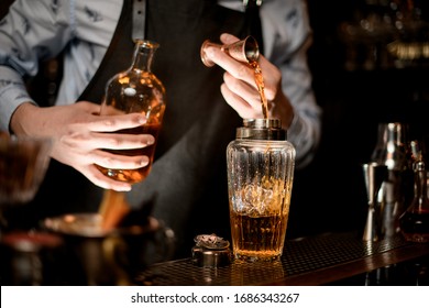 Close Up. Barman In Black Apron Carefully Pours Brown Alcoholic Drink To Glassy Shaker Using Beaker.