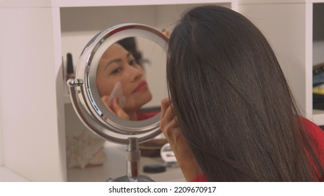 CLOSE UP: Blurred Mirror Reflection Of Lady Massaging Her Face With Jade Scraper. View Of Beautiful Asian Woman In Cosmetic Mirror Performing Anti-aging Massage Treatment With Gua Sha Scraper.