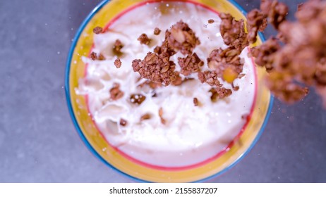 CLOSE UP, BOKEH: Top Down View Of Homemade Chocolate Granola Splashing In Milk. Tasty Chocolate Muesli In Shallow Focus Falling In Bowl Filled With Milk. Delicious Breakfast Assembly Caught In Motion.