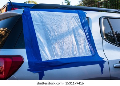 Close up. Broken and damaged car window temporarily covered with blue tape and plastic bag to protect interior from rain and water. Smash-and-grab automobile break-ins. Insurance concept. 