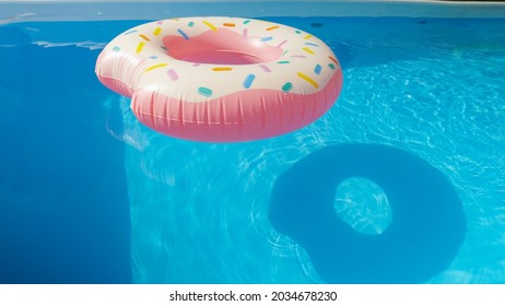 CLOSE UP: Colorful inflatable donut floats around the empty aqua colored pool in someone's backyard. Detailed shot of a plastic doughnut floatie drifting around the empty garden pool on a sunny day.