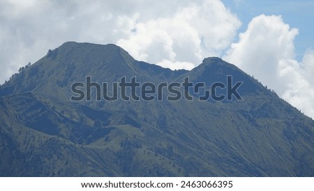 CLOSE UP: Colossal active volcano in Indonesia towering towards the cloudy sky. Breathtaking mountain scattered with trees shot from afar. Behemoth mountaintop of Mount Batur soaring through clouds.