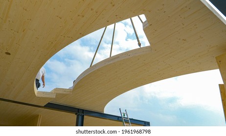 CLOSE UP: Contemporary CLT house is being assembled on a sunny spring day. Opening in the wooden ground of the top floor of a glued-laminated timber house offers a view of workers and clear blue skies