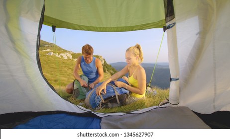 CLOSE UP: Cool Shot From The Inside Of A Tent Of A Cheerful Tourist Couple Setting Off On A Hike In The Beautiful Alps. Happy Girlfriend And Boyfriend About To Leave Their Tent And Go For A Short Trek