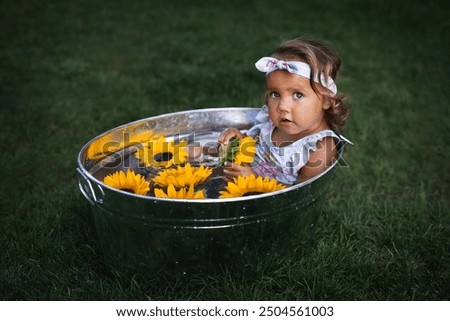 Close up, copy space. Cute baby girl take a bath in washtub with sunflowers outdoor.