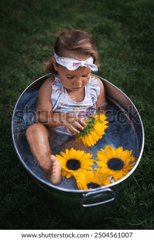 Close up, copy space. Cute baby girl play with sunflowers in washtub. She take a bath outdoor.