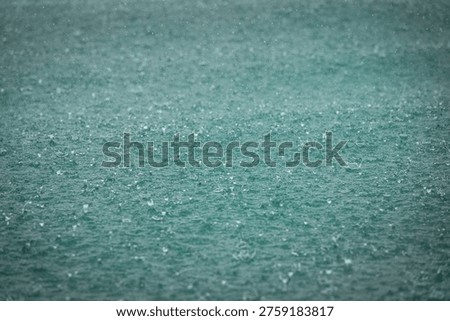CLOSE UP: Countless raindrops hit the sea during downpour, forming delicate splashes across the water. Clean, textural ocean background with tropical weather and muted color. Wet season in Indonesia.